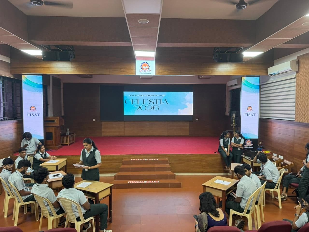 Quiz teams seated at desks in front of the stage as a quizmaster reads out a question, Celestia 2026 on the screen